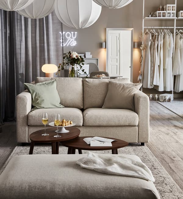 A wedding planner office featuring a light beige room setting with a light beige sofa, dark brown coffee table and an assortment of wedding dresses at the back of the room.