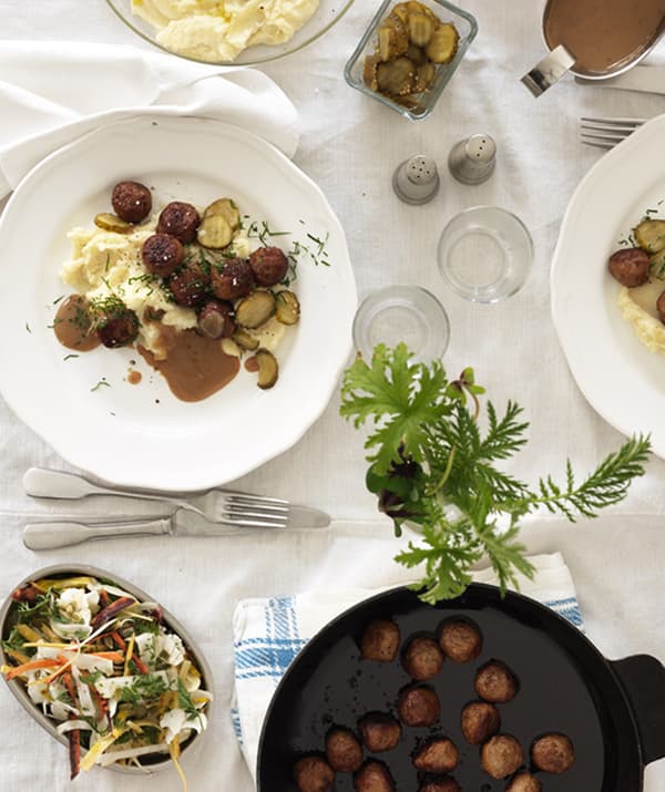 A well-laid table with a white tablecloth and two plates of meatballs with mashed potatoes and a side salad.