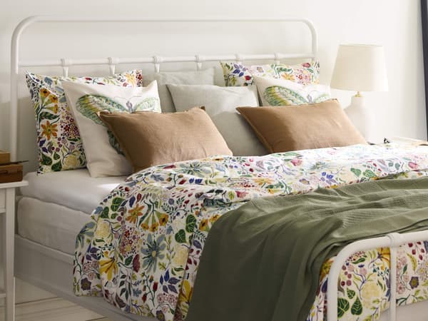 A well-made bed with colorful floral bedding and tan pillows in a bright room.
