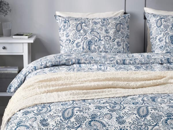 A well-made bed with white and blue paisley-designed bedding and pillows in a bright room.