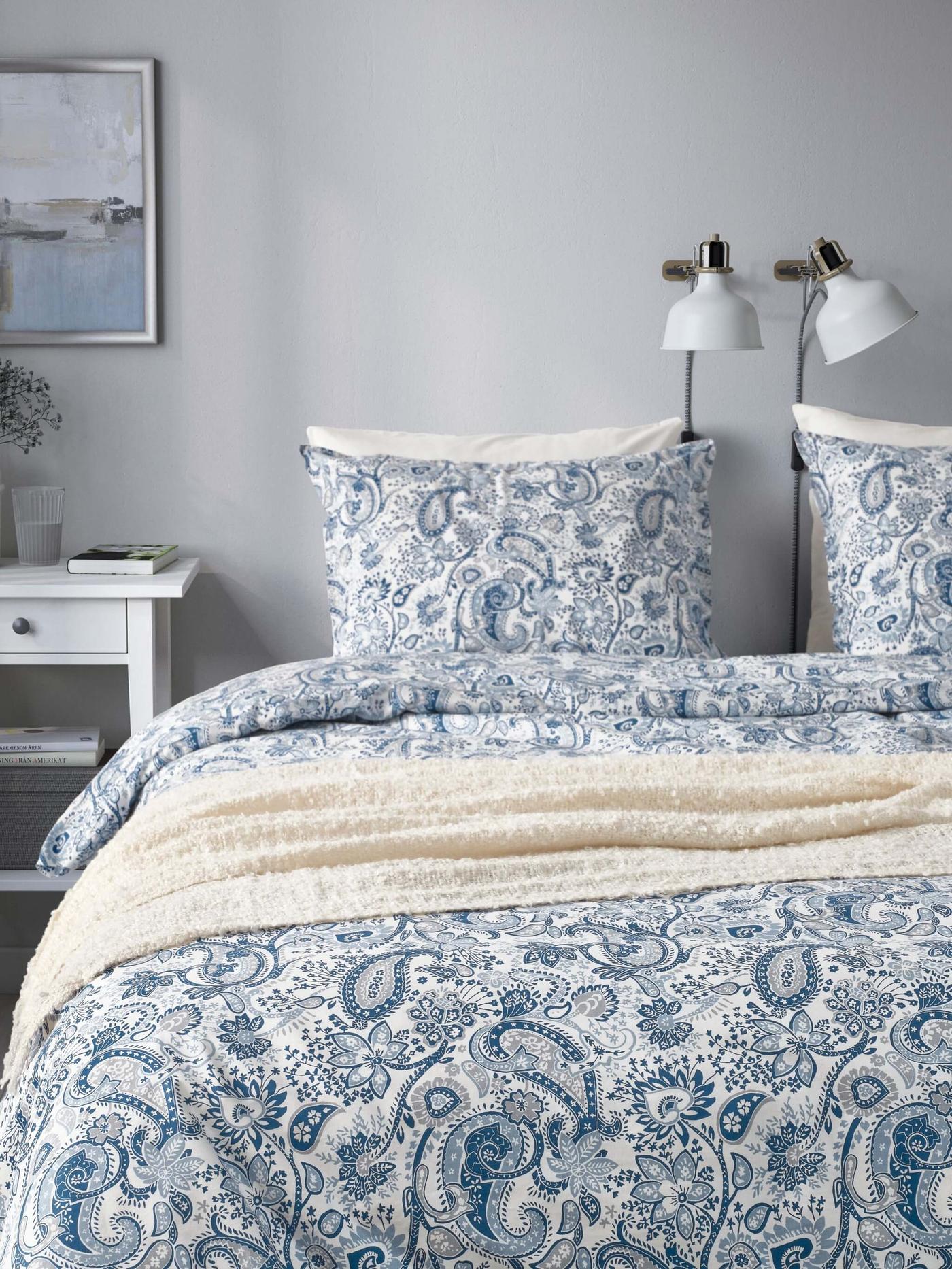A well-made bed with white and blue paisley-designed bedding and pillows in a bright room.