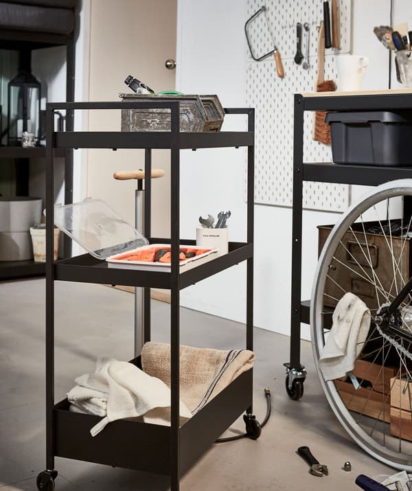 A wheeled trolley loaded with tools, placed on an open patch of floor next to a bike undergoing light repair work.