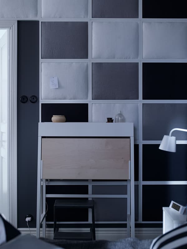 A white and birch IKEA PS bureau paired with white side tables and lamps in a bedroom.