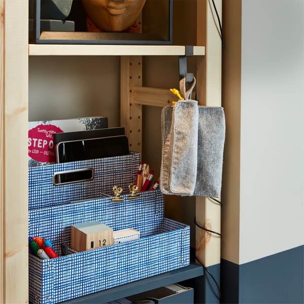 A white and blue IKEA FJÄLLA desk organizer on IVAR storage shelves, with an IKEA IVAR grey hook used to hang additional items.