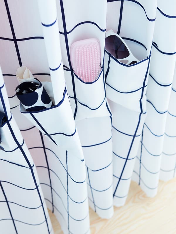 A white and blue ROSALILL curtain with sewn pockets for glasses, a brush and other small items.