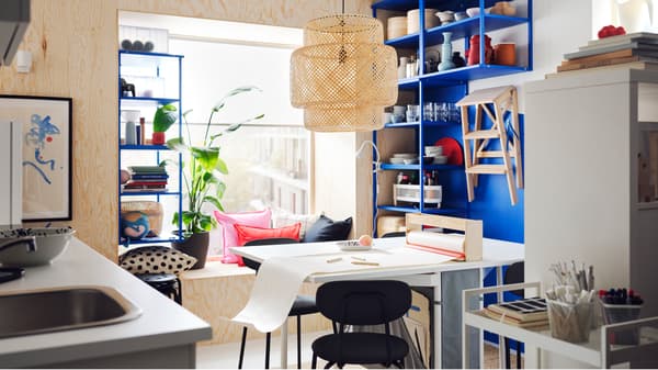A white and light grey KALLHÄLL gateleg table with storage and two ÖSTANÖ chairs in front of a PLATSA open shelving unit.