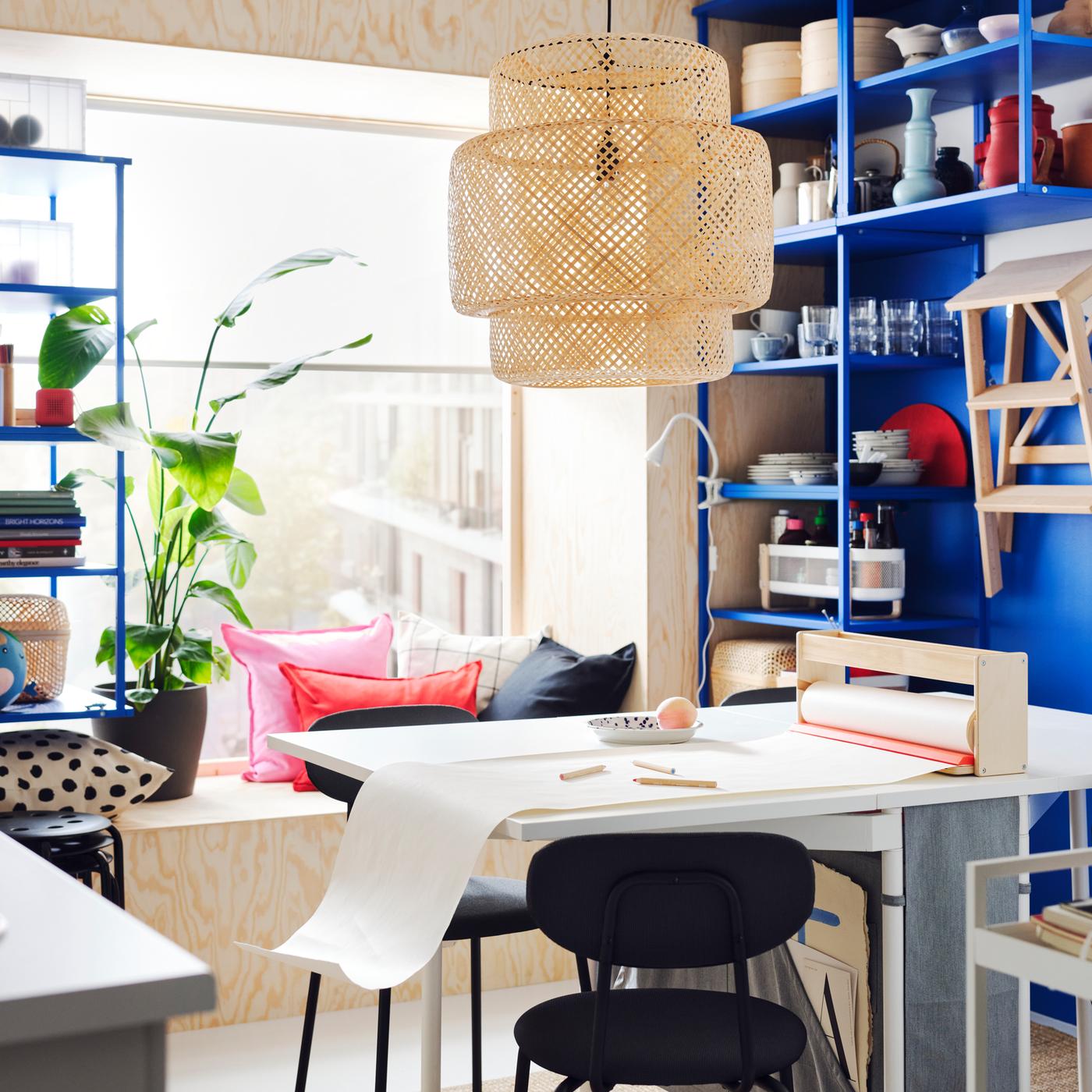 A white and light grey KALLHÄLL gateleg table with storage and two ÖSTANÖ chairs in front of a PLATSA open shelving unit.