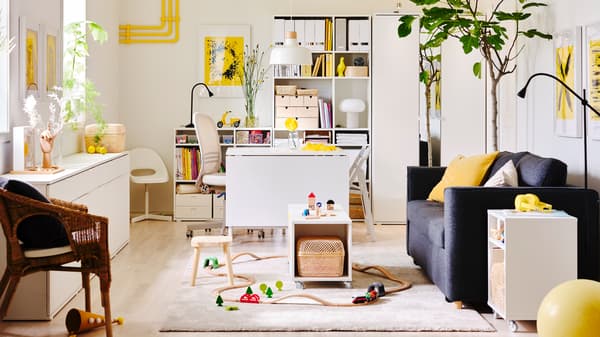 A white and yellow living room with white storage units and a dark grey PÄRUP sofa bed. Children's toys are on the floor.