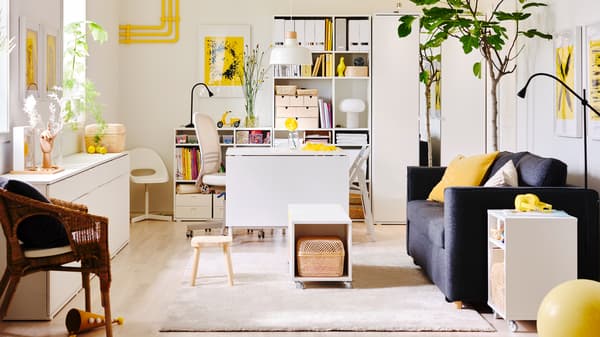 A white and yellow living room with white storage units and a dark grey PÄRUP sofa bed.