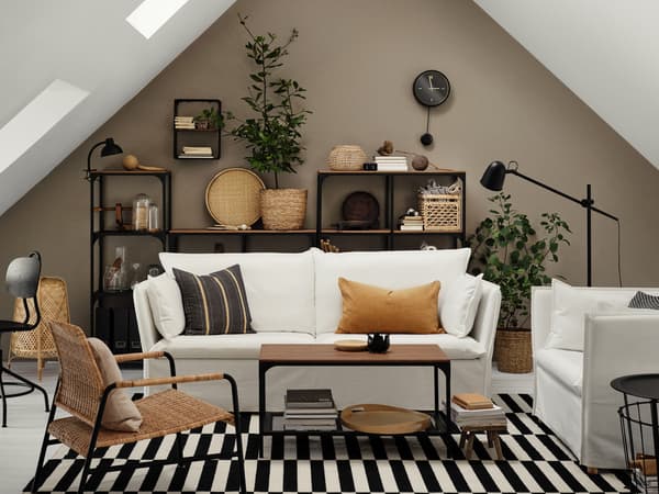 A white BACKSÄLEN three-seat sofa and other seating stand around a coffee table in an airy room with a high, pointed ceiling.