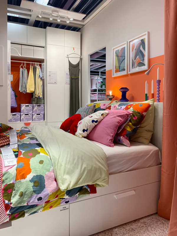 A white bed with drawers and colorful bedding with candles and a night light on the wide headboard