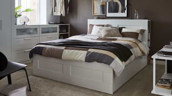 A white bed with headboard, brown patterned quilt cover and pillow cases, grey throw and cushions in white, grey and beige.
