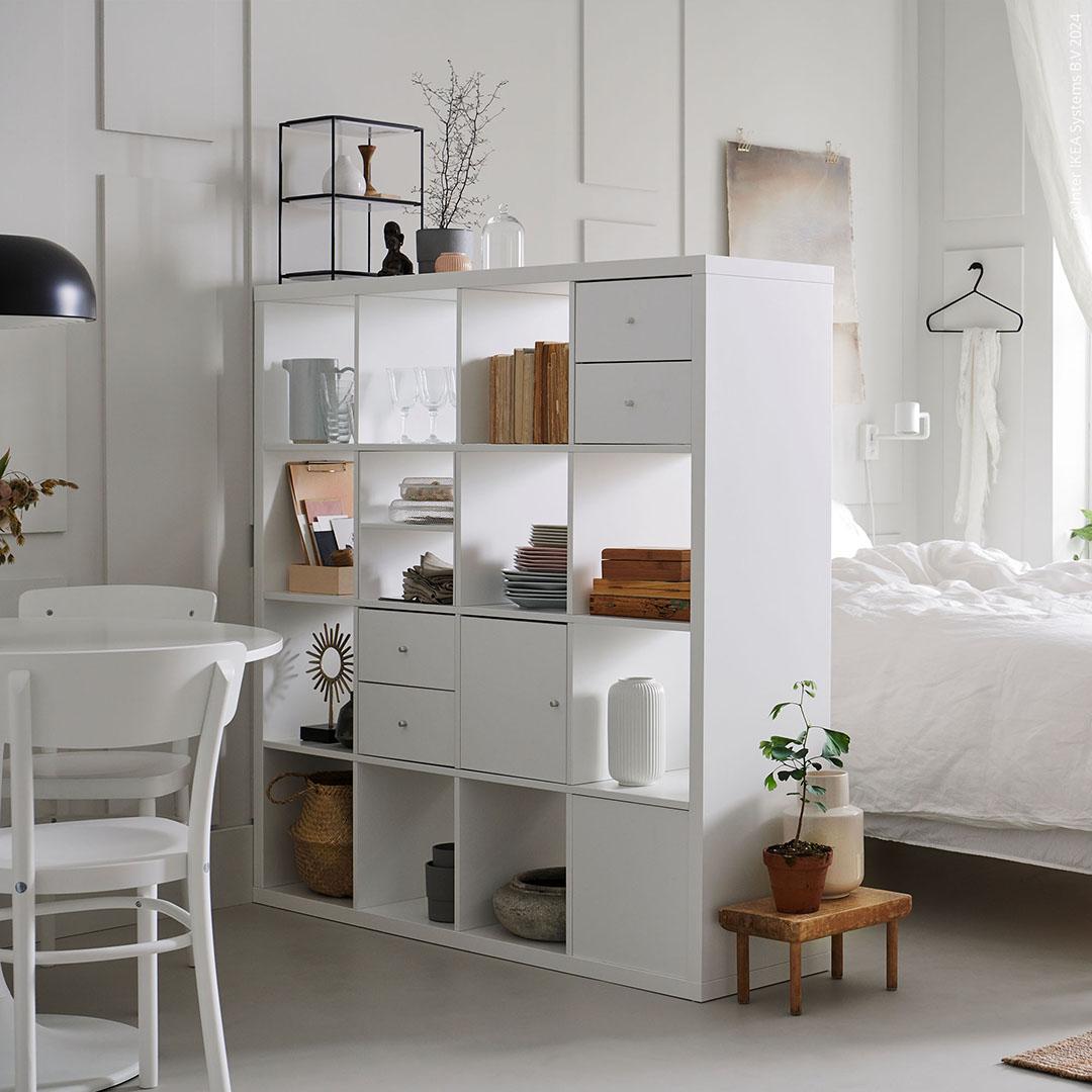 A white bedroom divided by cube storage to separate the dining area