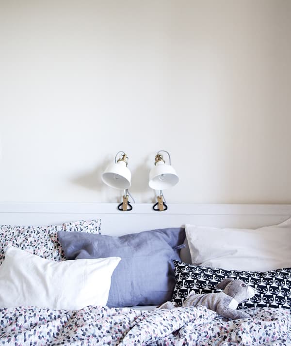 A white bedroom with two lamps clamped on the bed frame.