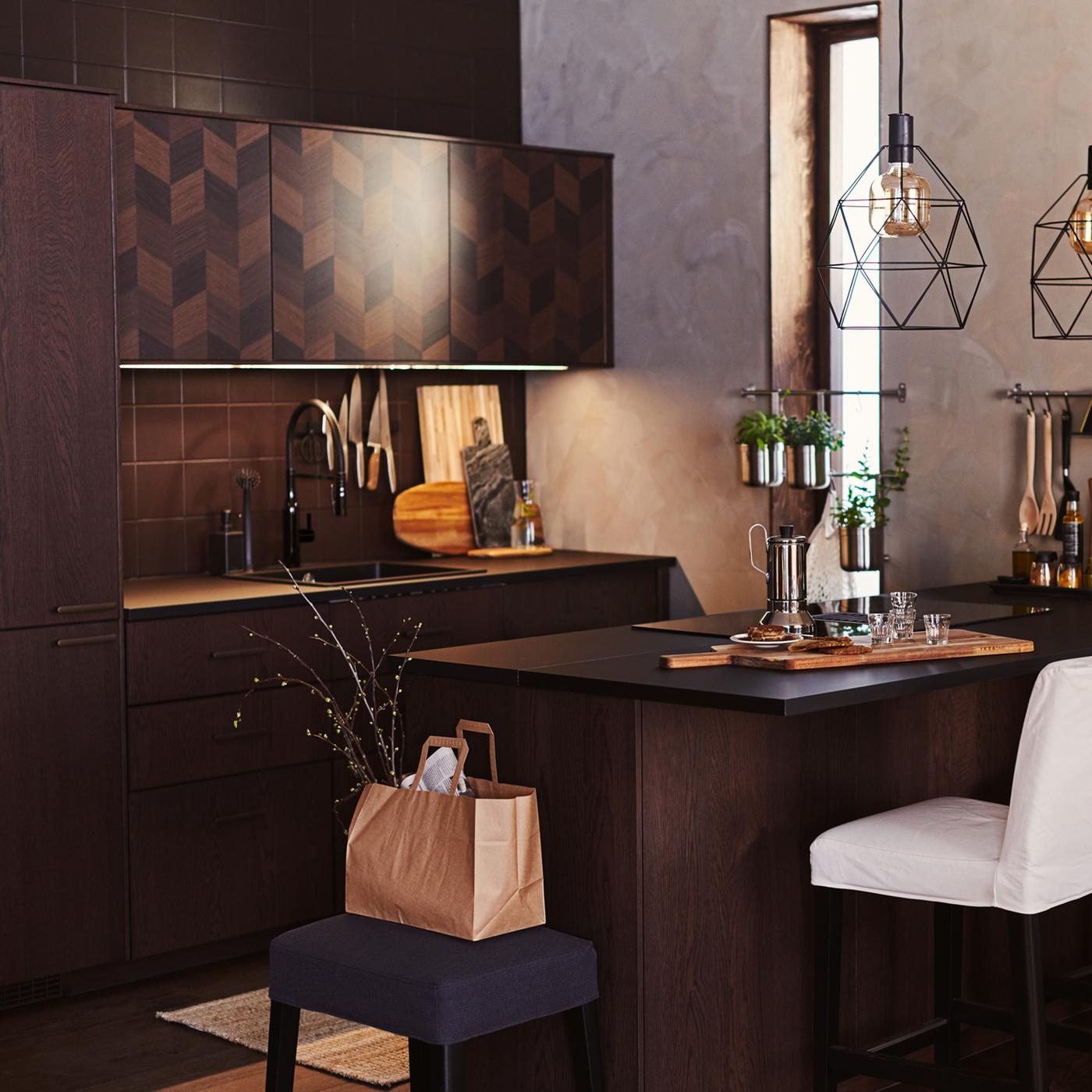 A white BERGMUND bar stool at an island worktop, two black BRUNSTA pendant lamps in a brown SINARP/HASSLARP kitchen.