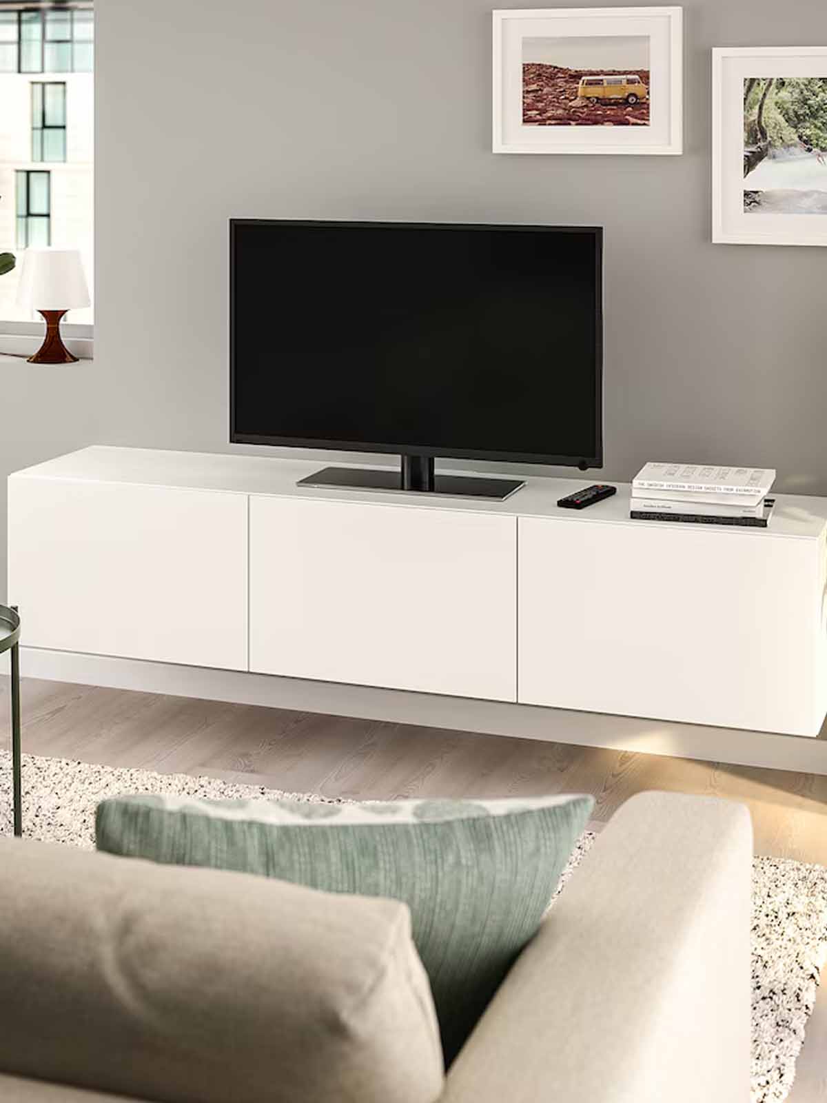 A white BESTA TV bench with a TV screen on top of it in the living room, in front of a white sofa.