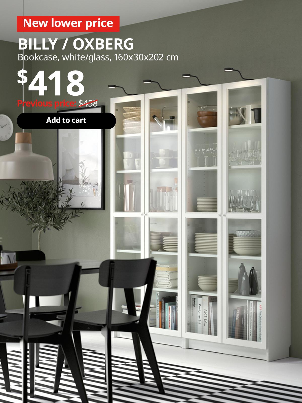 A white BILLY bookcase with white OXBERG white door frame with glass panel is placed in the dining room setting filled with tableware. Red 'Lower price' tag with white font on top left of image. White text reads "BILLY / OXBERG, Bookcase, $418." With previous price of $458 slashed.
