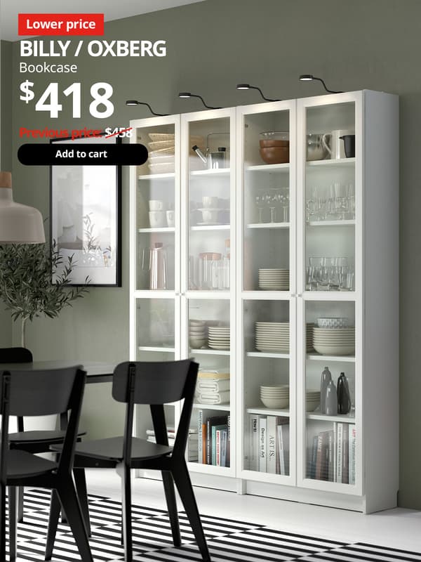A white BILLY bookcase with white OXBERG white door frame with glass panel is placed in the dining room setting filled with tableware. Red 'Lower price' tag with white font on top left of image. White text reads "BILLY / OXBERG, Bookcase, $418." With previous price of $458 slashed.