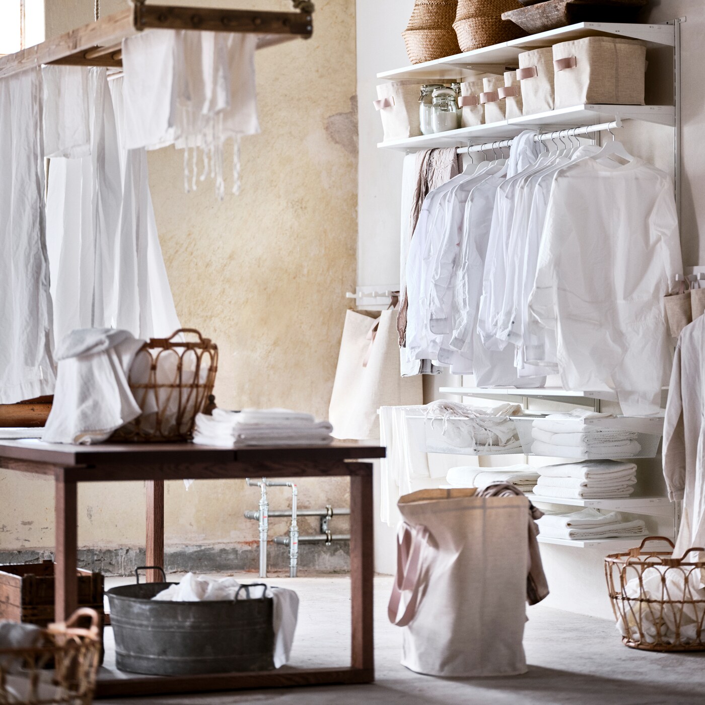 A white BOAXEL wardrobe combination with clothes on white hangers and storage baskets on top, plus a brown stained table.