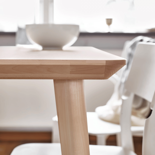 A white bowl on a wooden table, a white chair is partially tucked under the table.