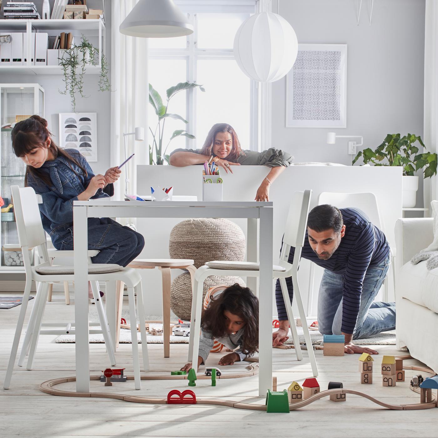 A white, bright living room with a four-person family engaged in playing with a LILLABO wooden train set.