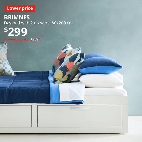 A white BRIMNES day-bed with 2 drawers is placed against the wall, with blue and white sheets and pillows on top. An red "Lower price" label is on the top left of the image with white text that reads: BRIMNES, Day-bed with 2 drawers, 80x200 cm, Price at $299, Previous price, $399.
