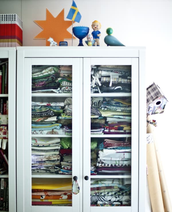 A white cabinet with glass doors filled with fabric.