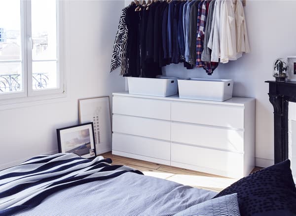 A white chest of drawers and clothes hanging in a bedroom.