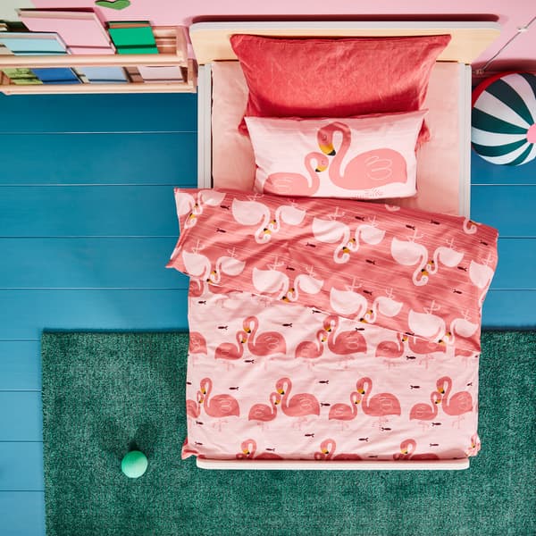 A white children’s bed frame with a pink bedsheet and bed textiles with flamingo patterns, a green rug and a round soft toy.