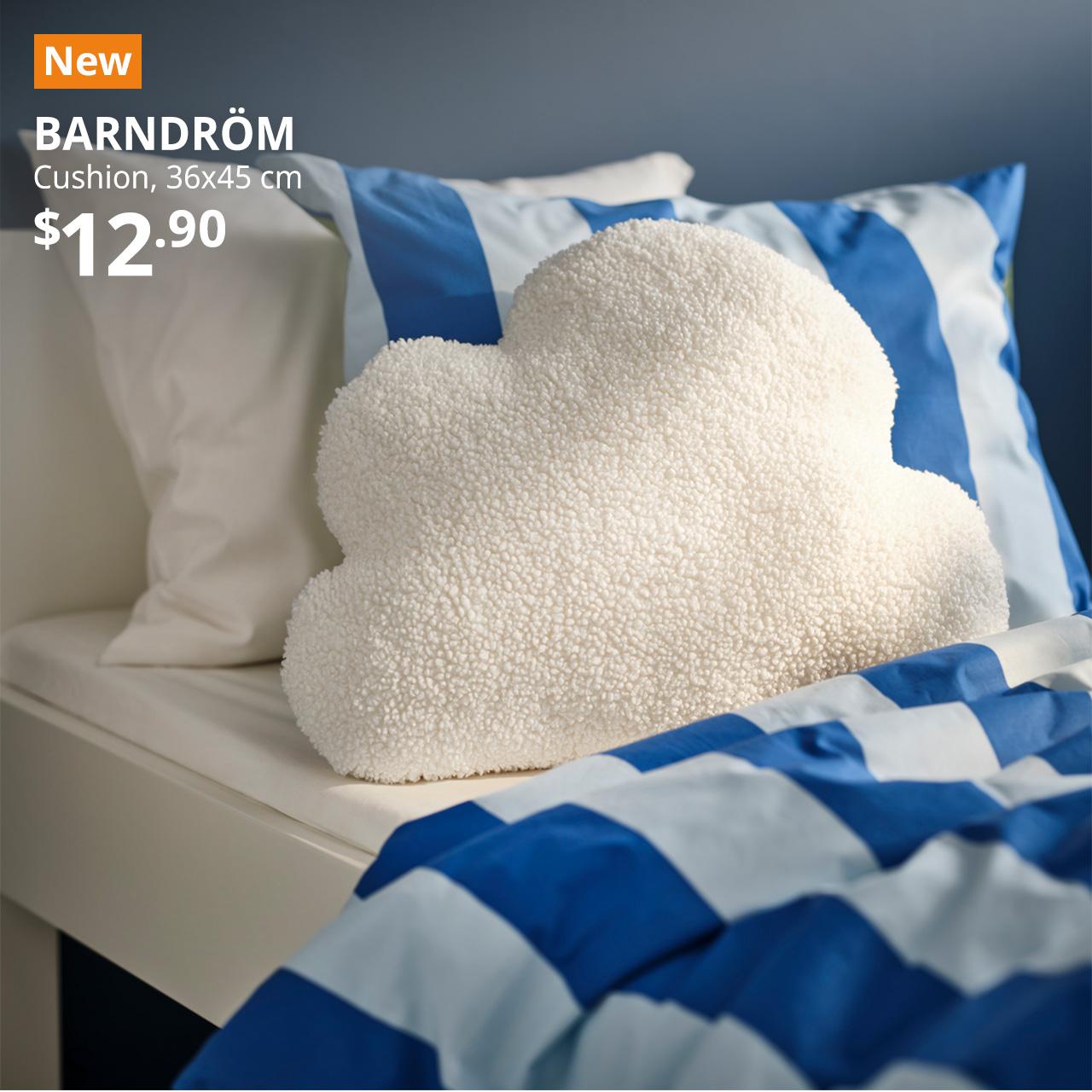 A white cloud-shaped BARNDRÖM cushion placed on a children's bed. A orange tag with white text that reads "New", followed by white text overlay image that reads, "BARNDRÖM, Cushion, 36x45 cm, $12.90".