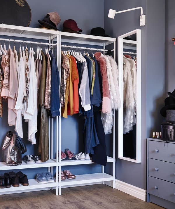 A white colored NISSEDAL wall-mounted mirror is placed beside the white framed clothing rack with a colorful clothes hanging on it.