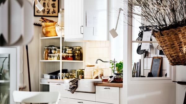 A white country-style kitchen with STENSUND fronts on METOD cabinets, a white sink and shelving with jars and utensils.