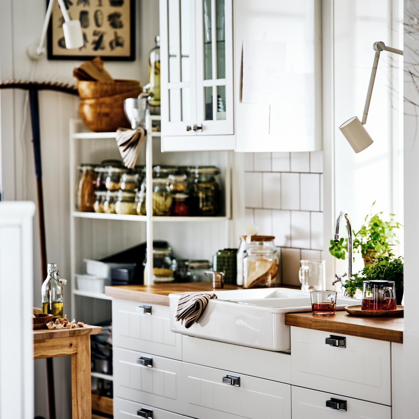 A white country-style STENSUND kitchen with a HAVSEN sink surrounded by open and closed shelving holding jars and cookware.