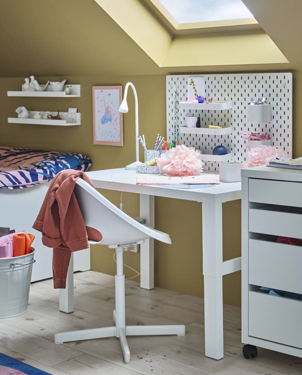 A white desk, a white junior swivel chair, a drawer unit, a wall-mounted pegboard with accessories and a white LED work lamp.