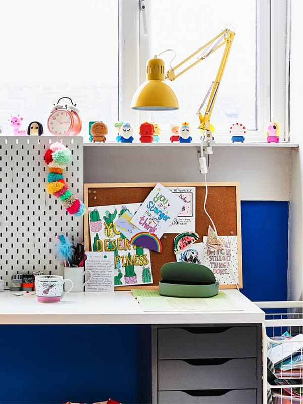 A white desk and yellow lamps against a blue wall, below a window.