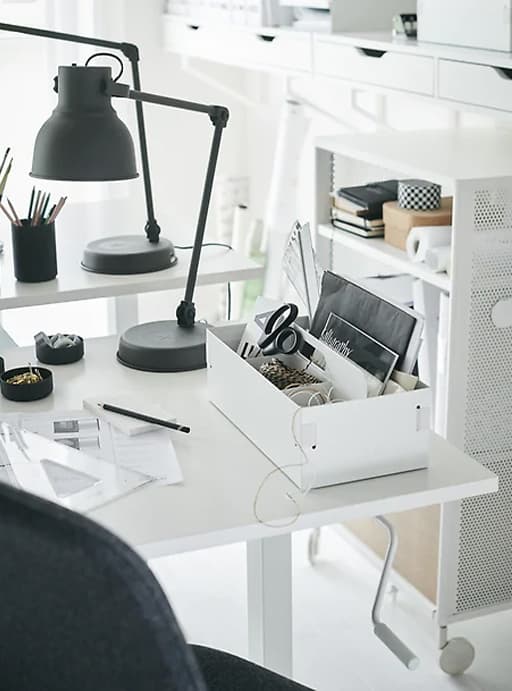A white desk with a desk tidy and a dark grey desk lamp.