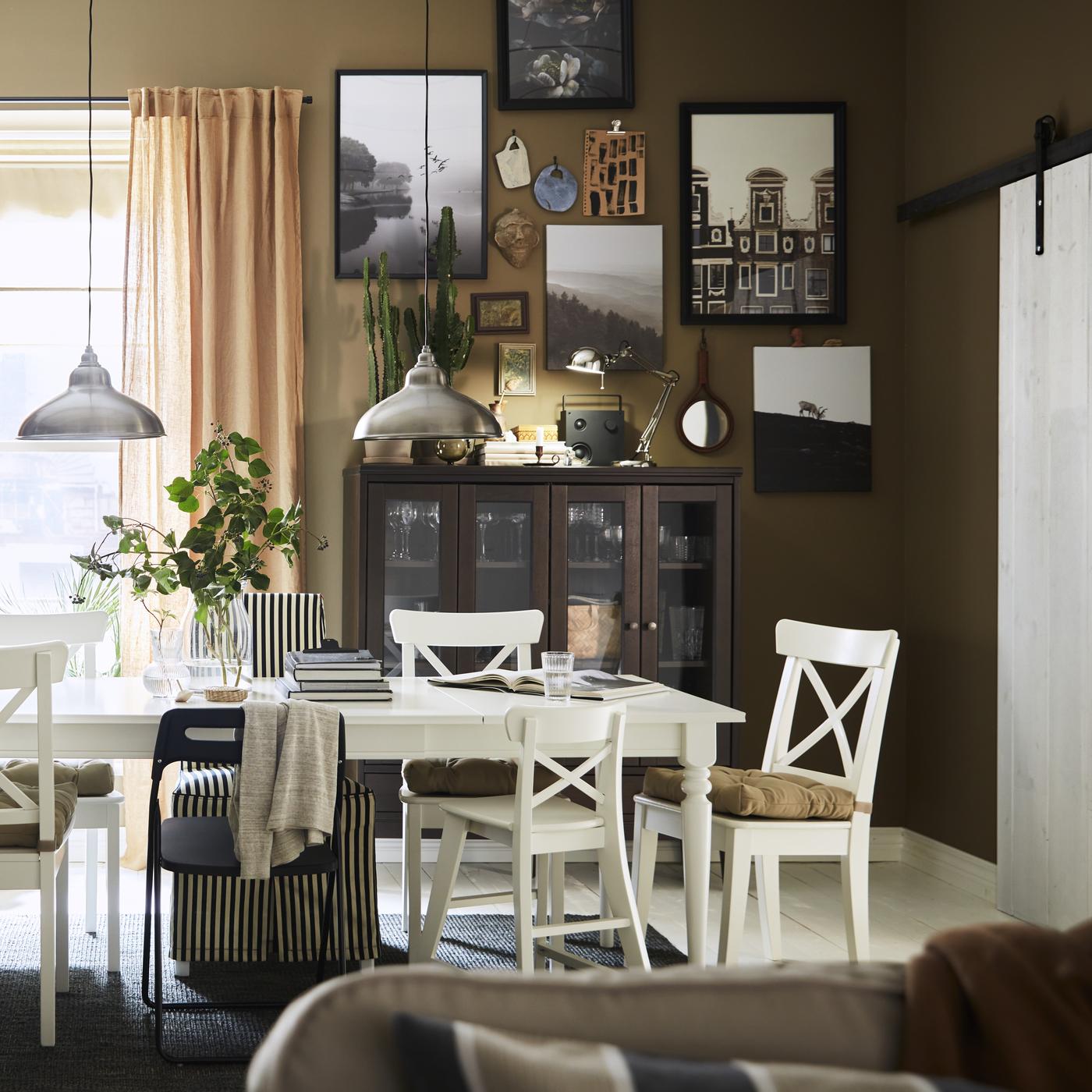 A white dining room table and chairs with multiple images framed hanging on the wall in the background.