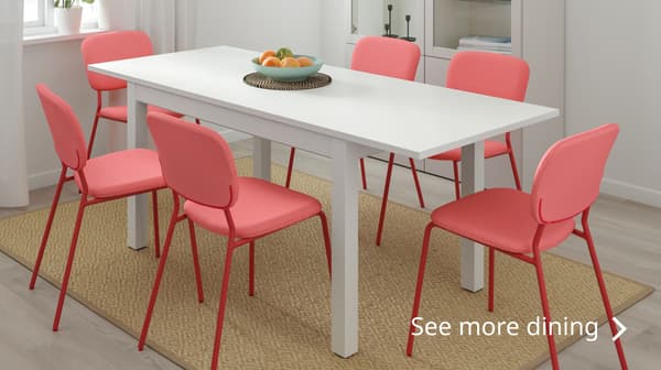 A white dining table and six red chairs around it. A mat is placed below the dining table and chairs. Text reads: See more dining >