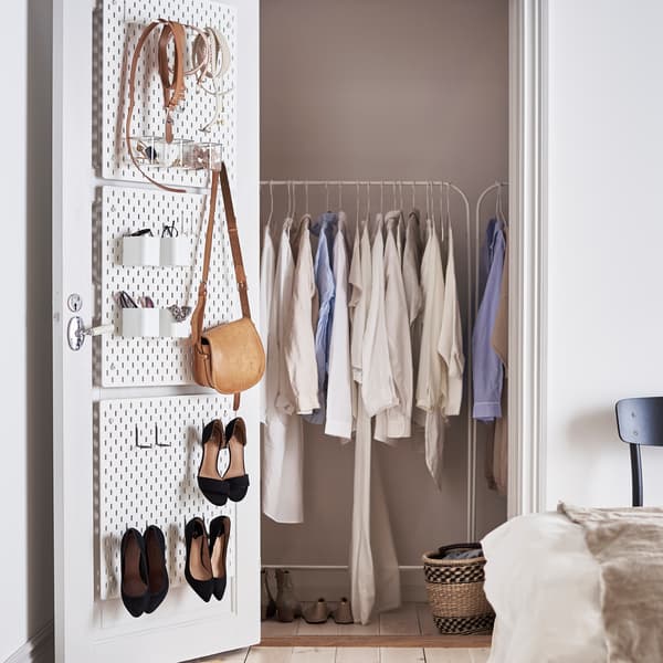 A white door with SKÅDIS pegboard, on which hang a bag and shoes. In the closet is a clothes rack with clothes