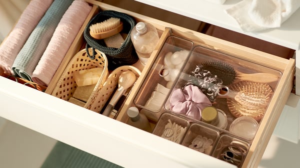 A white drawer opened to reveal clear plastic storage containers and baskets for bathroom accessories.