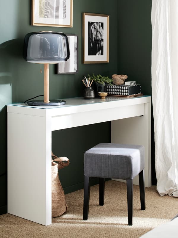 A white dressing table, a grey table lamp, a grey and black stool and gold-coloured frames.