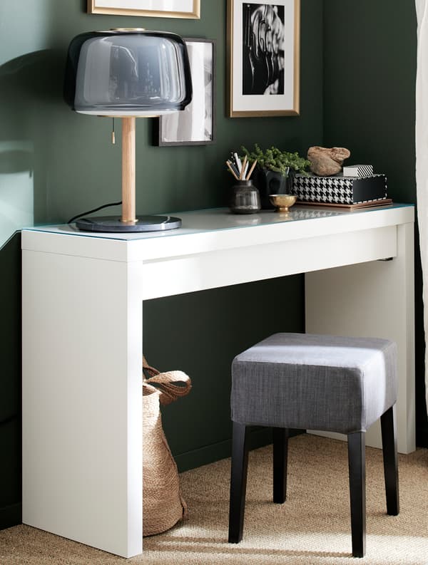 A white dressing table, a grey table lamp, a grey and black stool and gold-coloured frames.