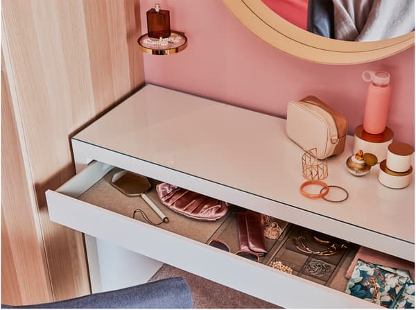 A white dressing table, a round mirror, a wardrobe in white stained oak effect and a metal/glass display shelf.