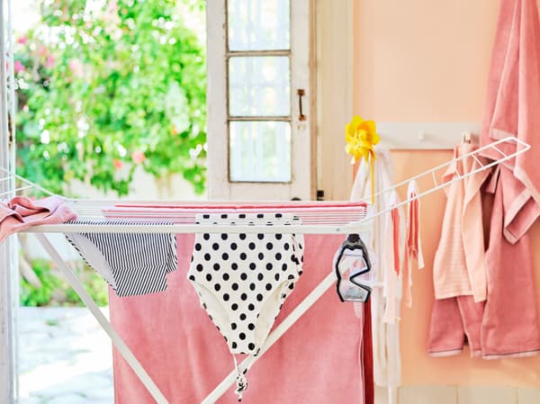 A white drying rack filled with clothing in coral and black and white. Swimming goggles are also hanging on the rack.