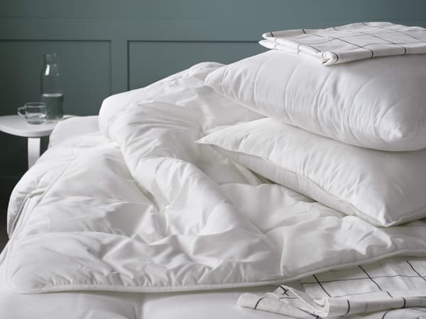 A white duvet inset sitting on a bed with white pillows on top.