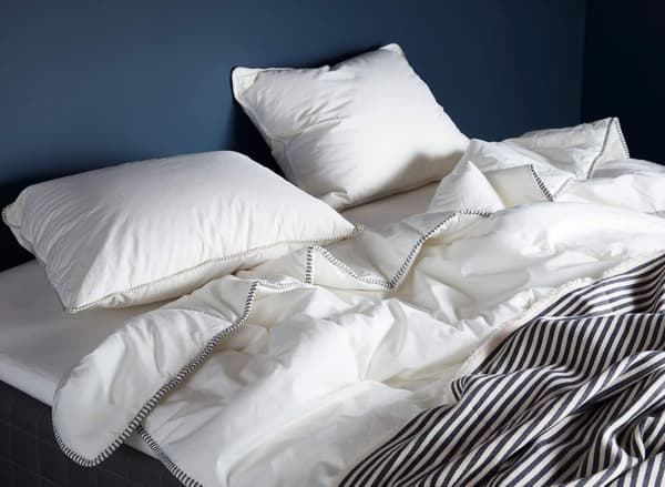 A white duvet with two white pillows on a bed against a blue wall. Go to comfort guide