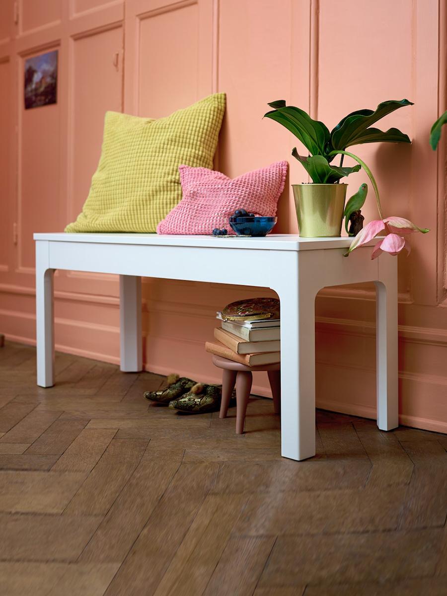 A white EKEDALEN bench is placed alongside a hallway, with cushions and plants on it.