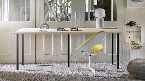 A white ELLOVEN monitor stand with drawer with a computer on top of it, on a desk in a white-toned workspace.