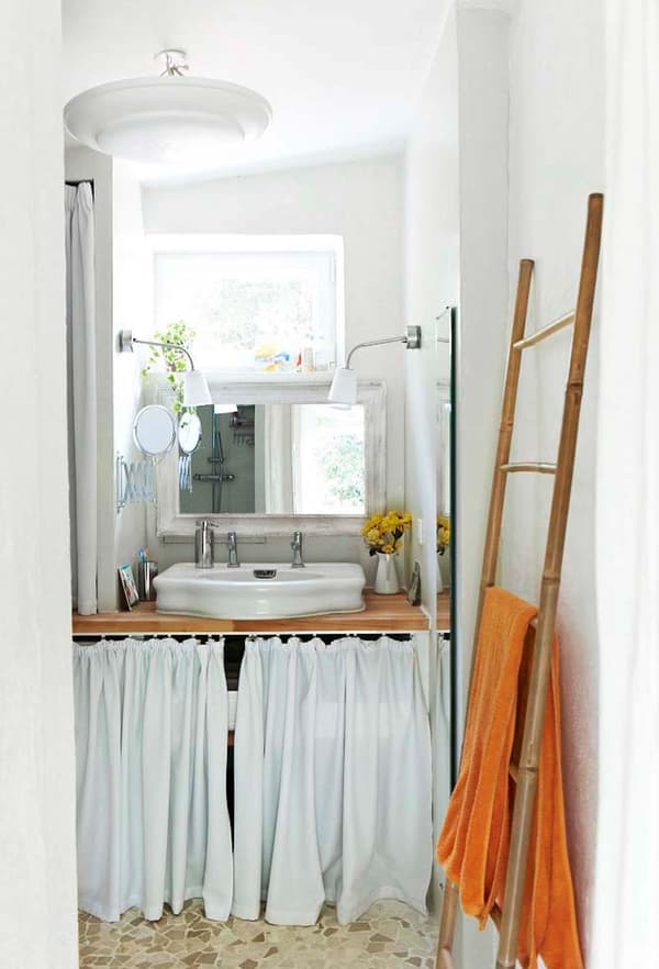 A white fabric curtain hide bathroom essentials under the bathroom sink in a small, white bathroom.