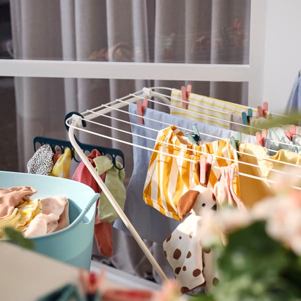 A white FROST drying rack for outdoor and indoor use placed on a balcony. Clothes in different colours hang on the rack. 